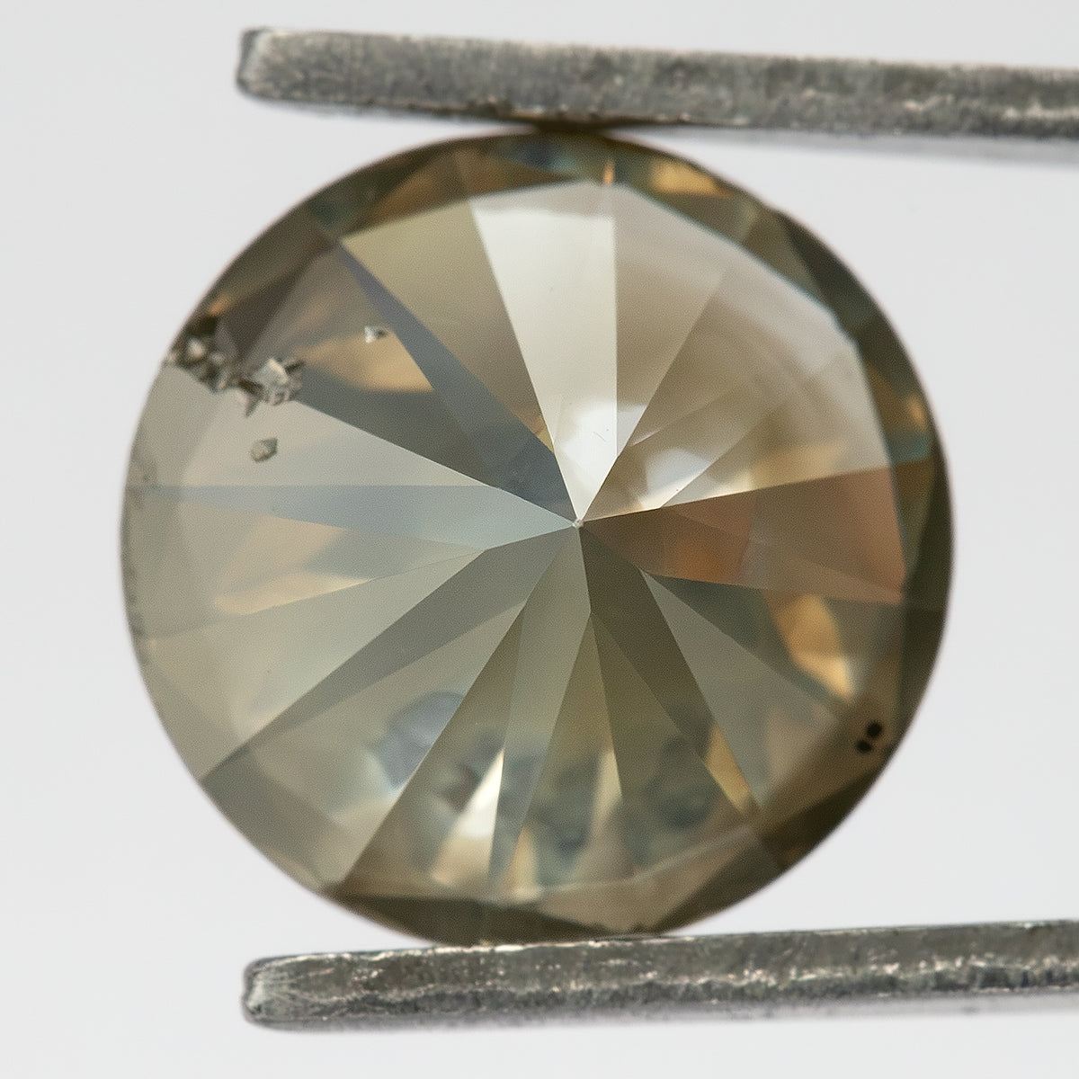 Close-up of the underside of KL444 in tweezers, showing broad pavilion facets and cavities near the upper-left edge.