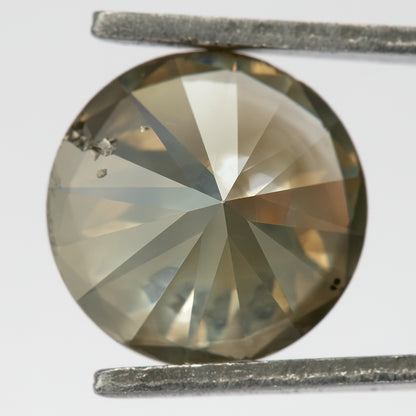Close-up of the underside of KL444 in tweezers, showing broad pavilion facets and cavities near the upper-left edge.