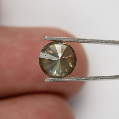 Smaller back view of KL444 held in tweezers against a fingertip, showing its pavilion facet pattern.
