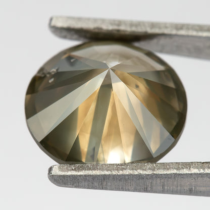 Angled pavilion view of KL444 in tweezers, showing the pointed underside, facet reflections and cavities near the edge.