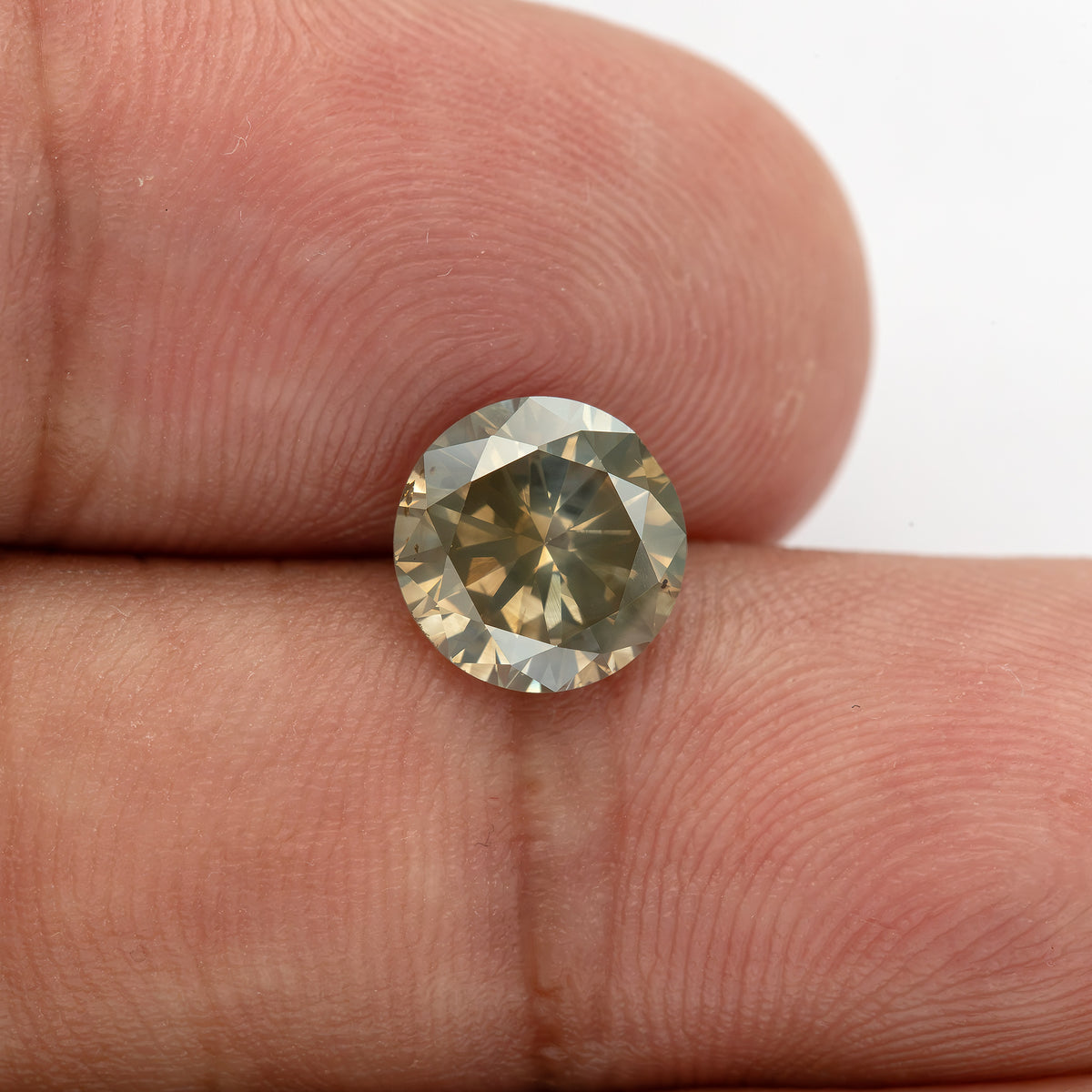 Close view of KL444 resting against fingertips, showing its round face-up outline and warm brown reflections.