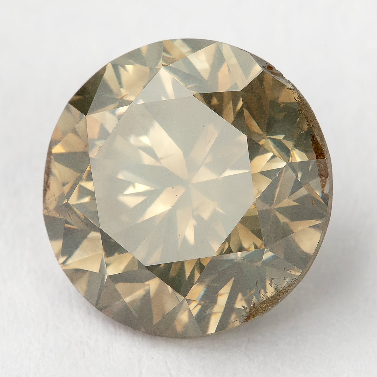 Bright rotated face-up macro of the round brilliant diamond, with a pale champagne center, olive-gray edge reflections and irregular brown features visible along the right and lower girdle.
