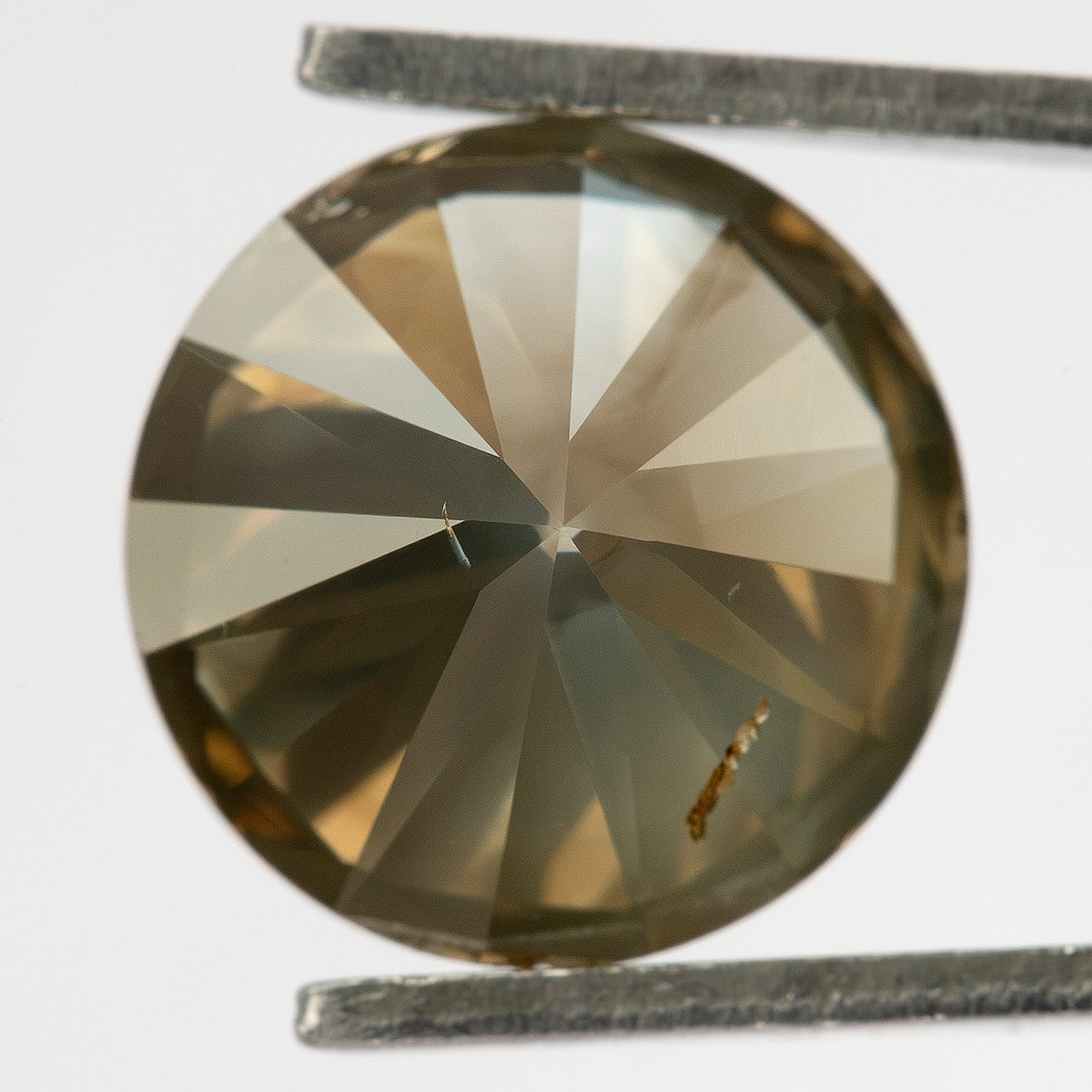 Straight-on pavilion macro of the round brilliant diamond, showing its radial pavilion facets, muted olive-gray and champagne reflections, and an elongated brown feature near the lower-right area.