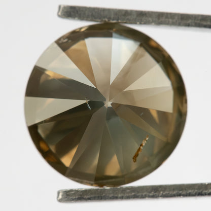 Straight-on pavilion macro of the round brilliant diamond, showing its radial pavilion facets, muted olive-gray and champagne reflections, and an elongated brown feature near the lower-right area.