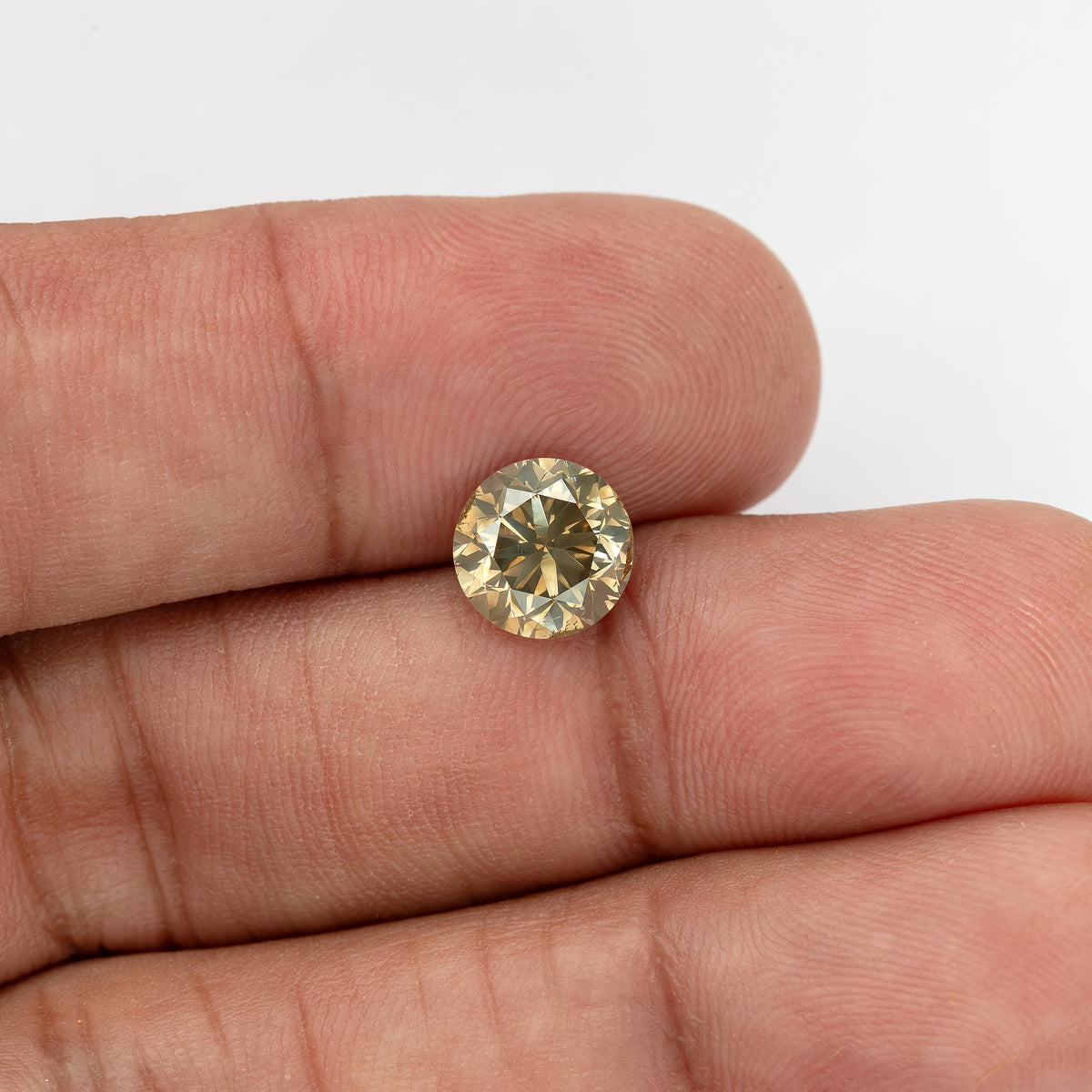 Wider hand-scale view of the round brilliant diamond on fingertips, showing its round outline, pale-yellow champagne flashes, olive-gray center and visible girdle features.