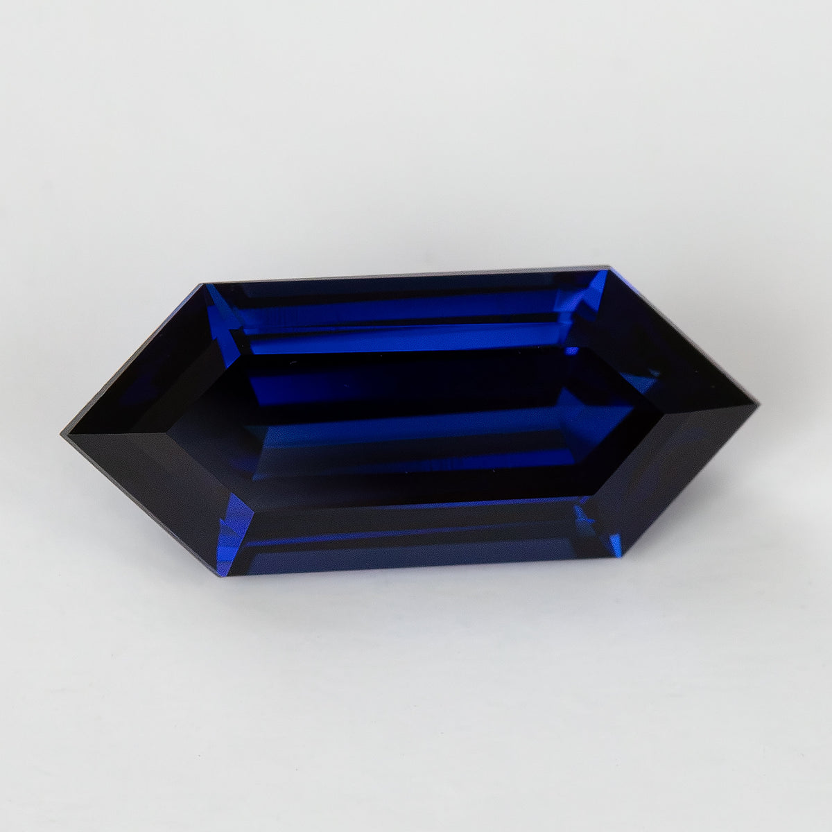 Horizontal face-up view of the deep-blue elongated hexagonal sapphire, showing dark central facets and bright blue step reflections.