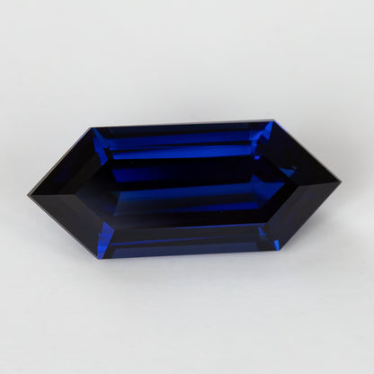 Horizontal face-up view of the deep-blue elongated hexagonal sapphire, showing dark central facets and bright blue step reflections.