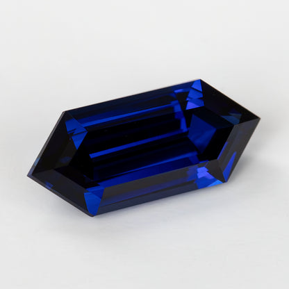 Angled face-up view of the elongated blue sapphire, showing pointed ends and bright blue bands within darker facets.