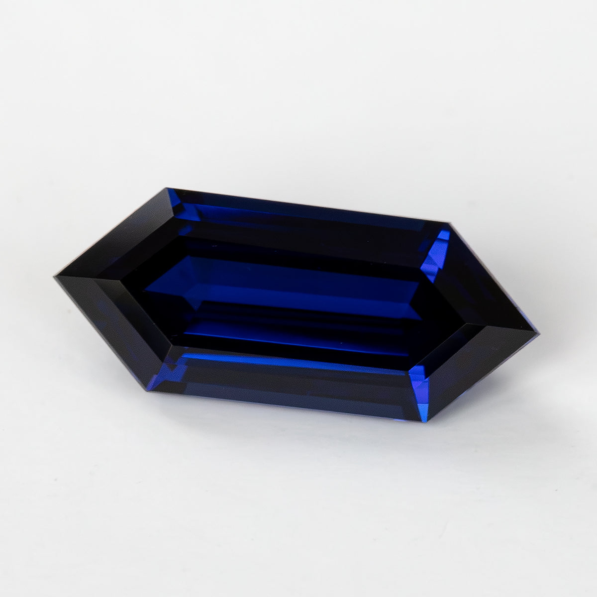 Low angled face-up view showing long blue step facets and the hexagonal outline against a light background.