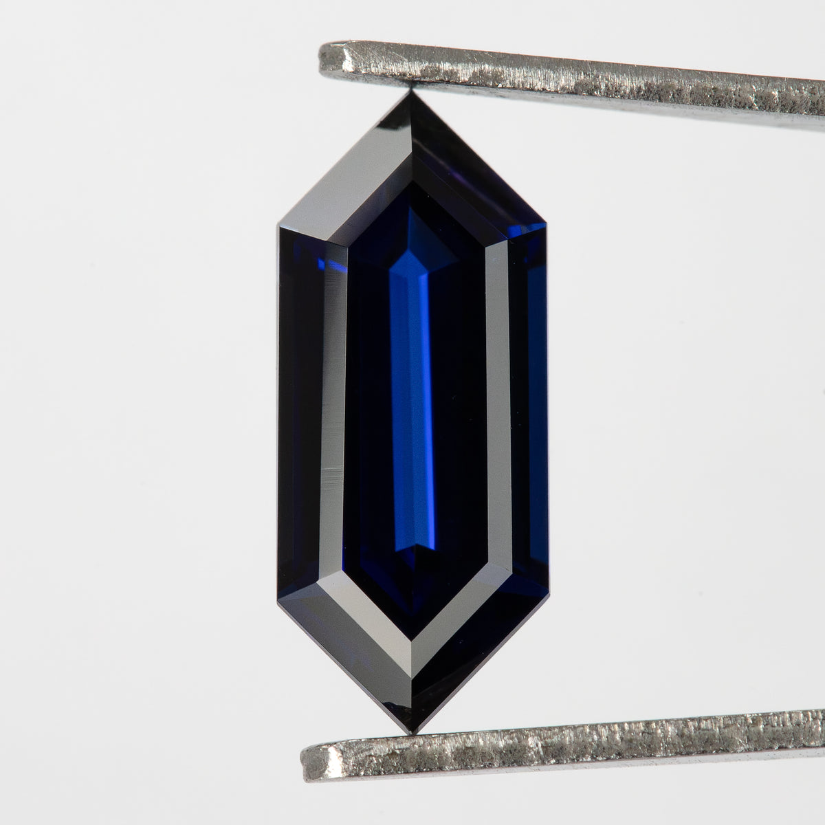 Vertical broad-face view in tweezers, showing pointed ends and long dark and blue facet bands.