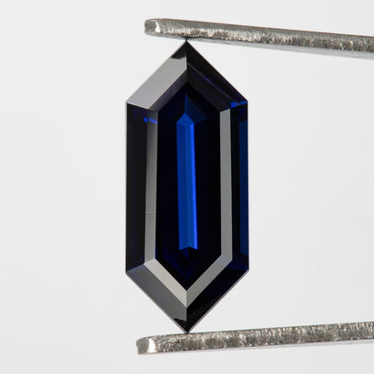 Vertical broad-face view in tweezers, showing pointed ends and long dark and blue facet bands.