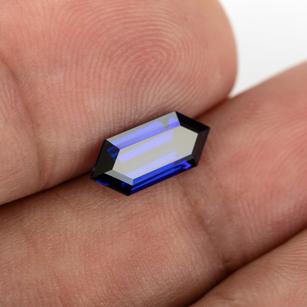 Blue sapphire resting between fingertips with a pale reflection across its broad center.