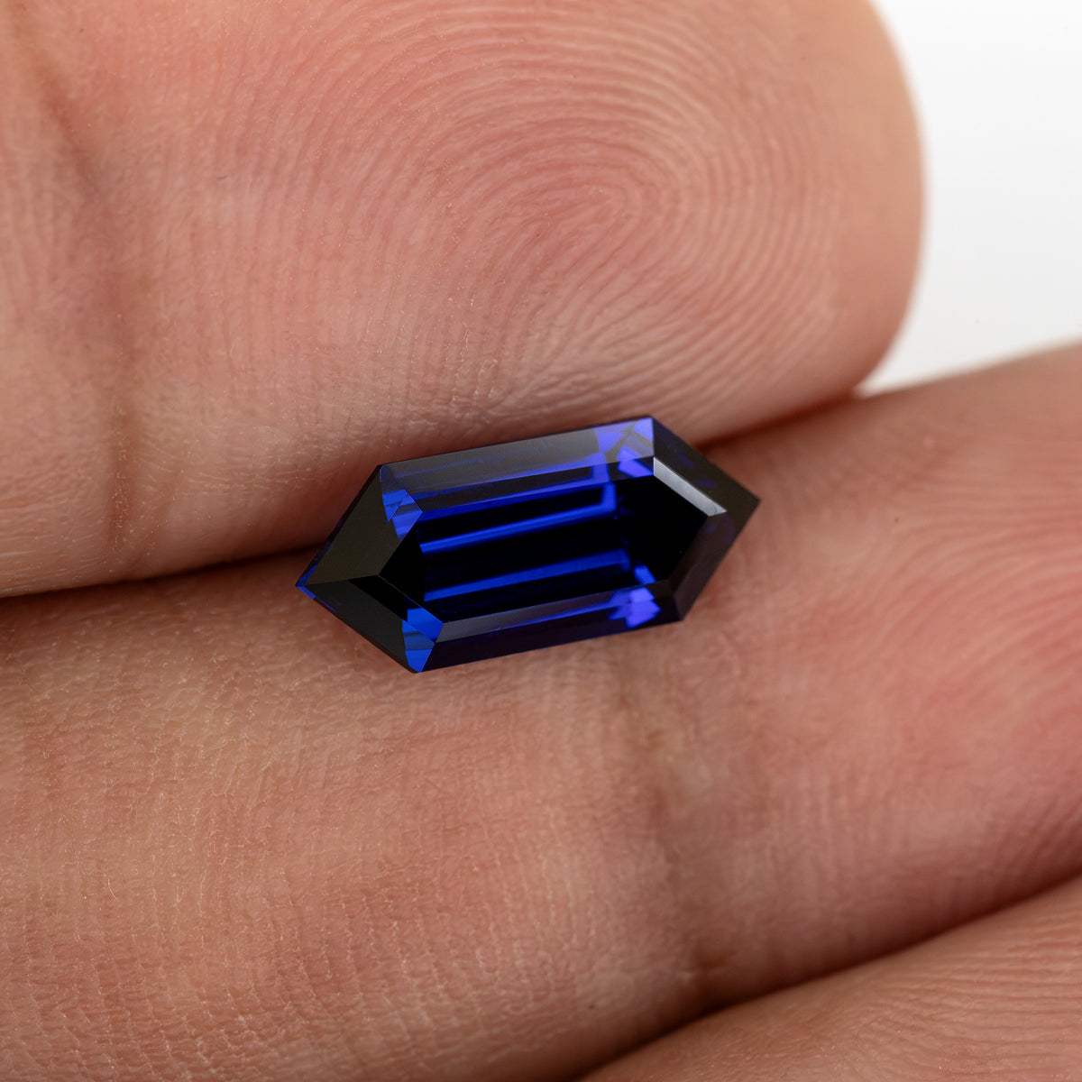 Blue hexagonal sapphire on fingertips, with dark center and bright blue step reflections.