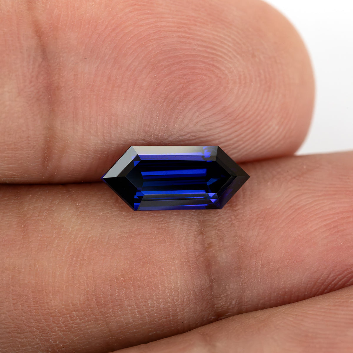 Horizontal fingertip-scale view of the sapphire’s long pointed-end outline and blue stepped interior.