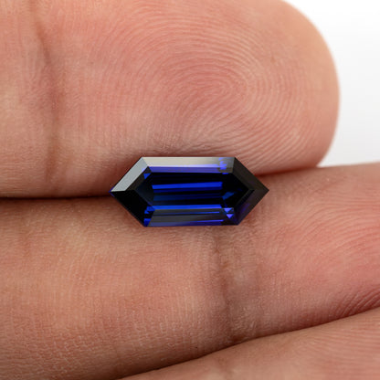 Horizontal fingertip-scale view of the sapphire’s long pointed-end outline and blue stepped interior.