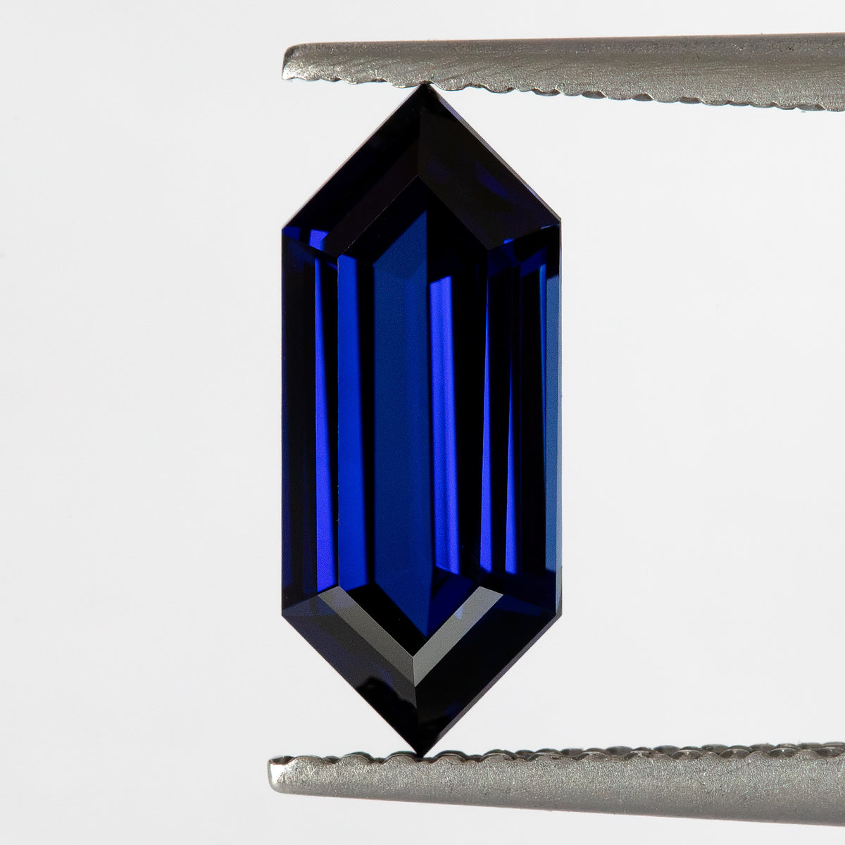 Upright tweezers view from another tilt, showing the long sapphire’s blue center and pointed ends.