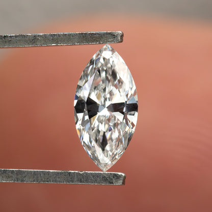One marquise diamond held vertically face-up in tweezers in front of a finger, showing pointed ends and bright brilliant facets.