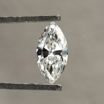 Single marquise diamond held face-up in tweezers against a neutral gray background, with white and dark reflections across its crown.