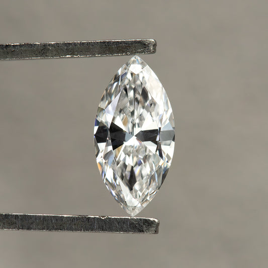 Single marquise diamond held face-up in tweezers against a neutral gray background, with white and dark reflections across its crown.