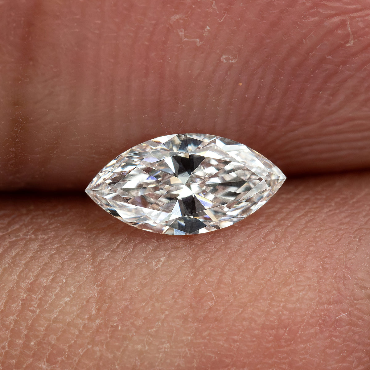 One marquise diamond resting horizontally between fingertips, with skin texture showing the scale of the representative stone.