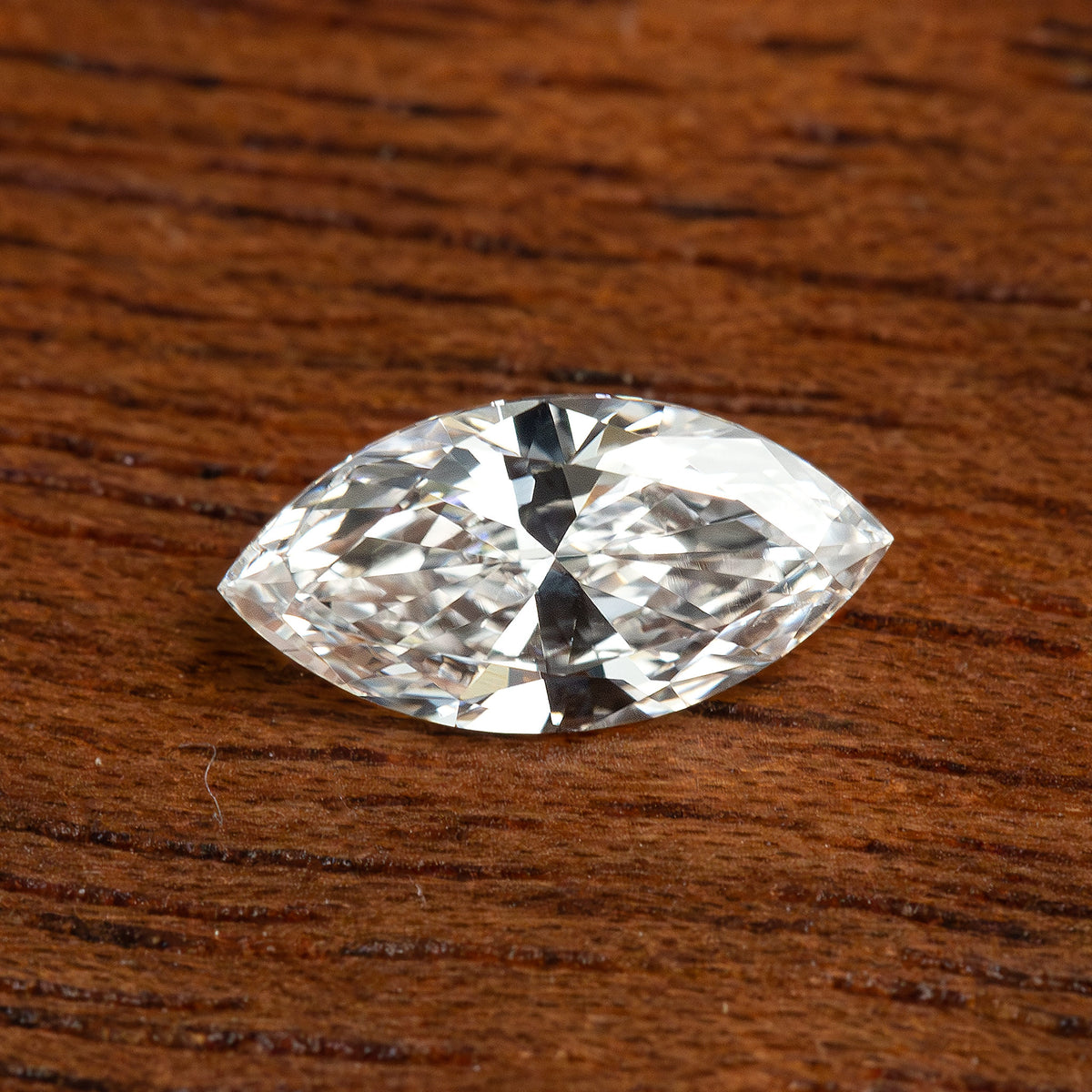 Single marquise diamond lying face-up on a wooden surface, with brilliant white reflections and darker central facets.