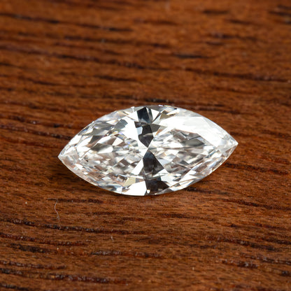 Single marquise diamond lying face-up on a wooden surface, with brilliant white reflections and darker central facets.
