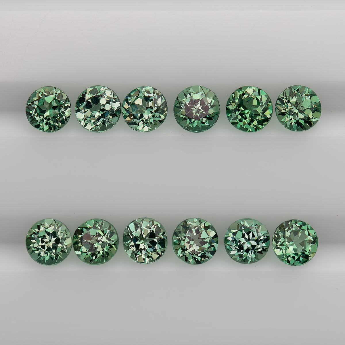Representative mint-green round lab-grown sapphire stock arranged table-up in two rows, showing flower-style faceting; sold per stone.