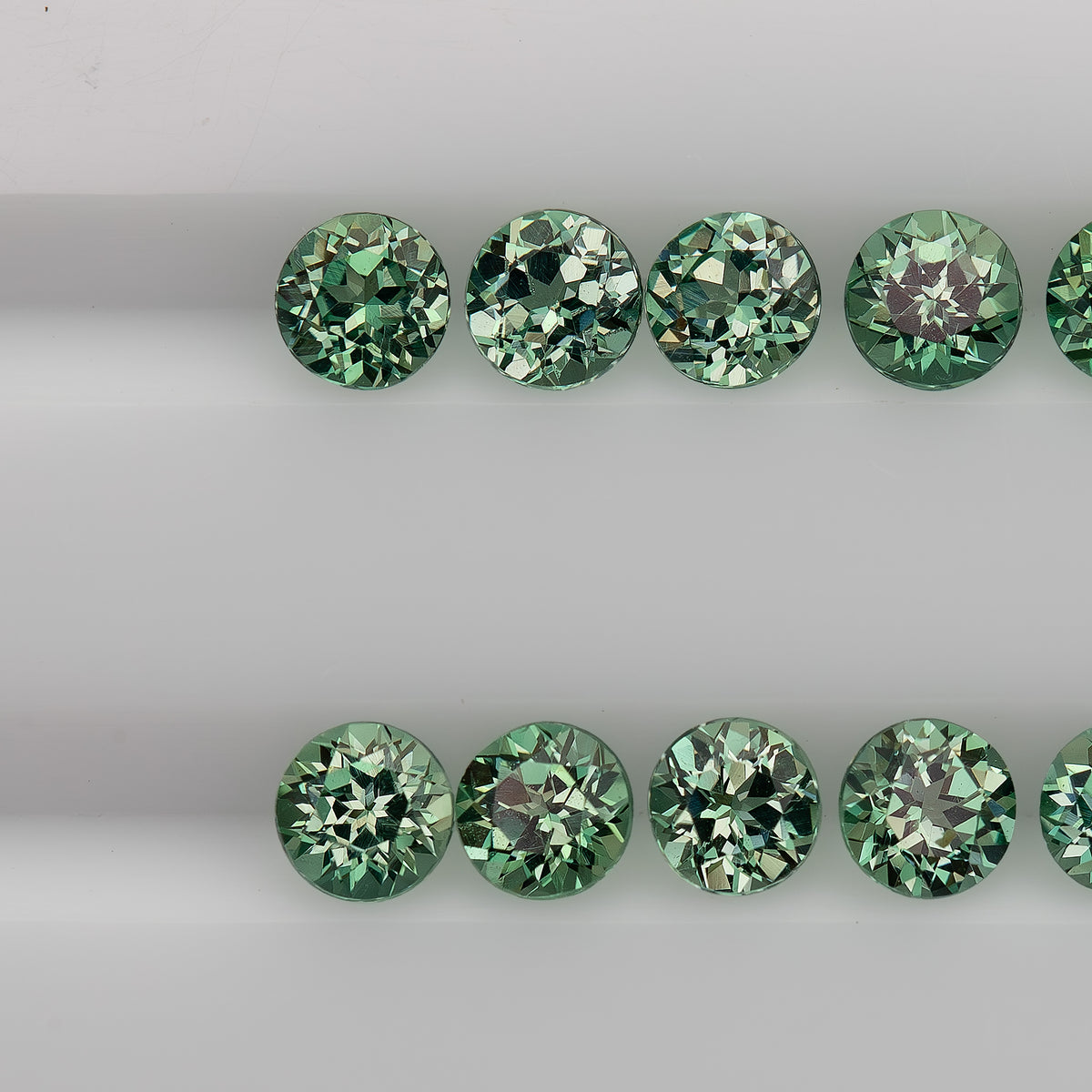 Macro view of mint-green round sapphire stock in two table-up rows, showing varied flower-style reflections.