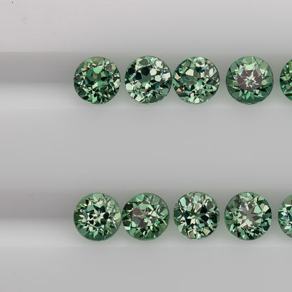 Macro view of mint-green round sapphire stock in two table-up rows, showing varied flower-style reflections.