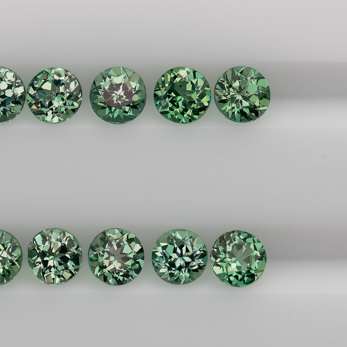 Close table-up rows of mint-green round lab-grown sapphires with alternating pale and dark facet reflections.