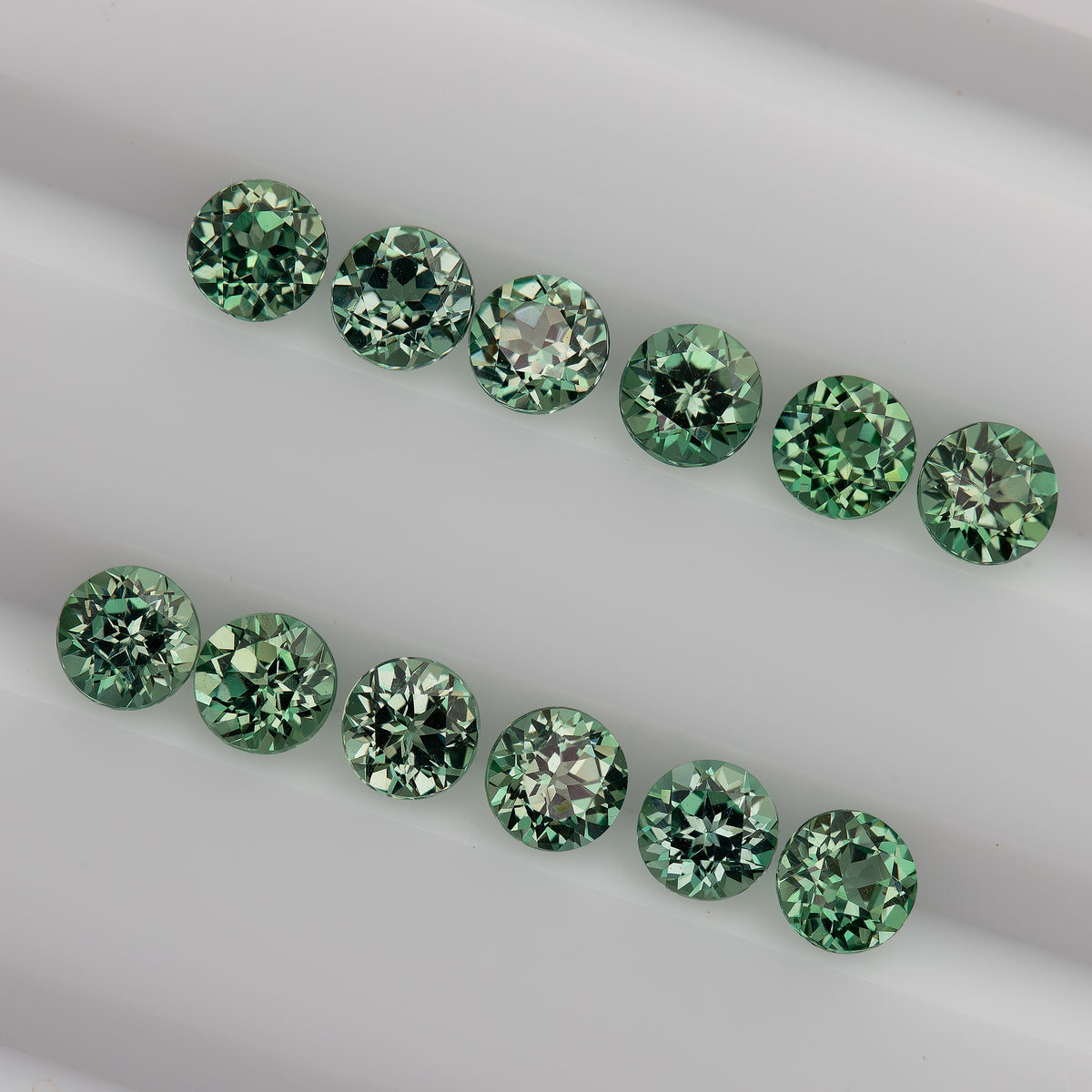 Mint-green round sapphire stock seen obliquely in two rows, with tables and crown facets still visible.