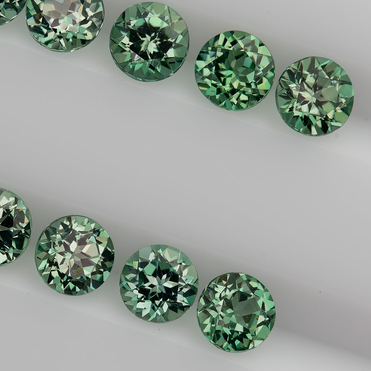 Oblique macro view of two rows of mint-green round lab-grown sapphires on a white tray.