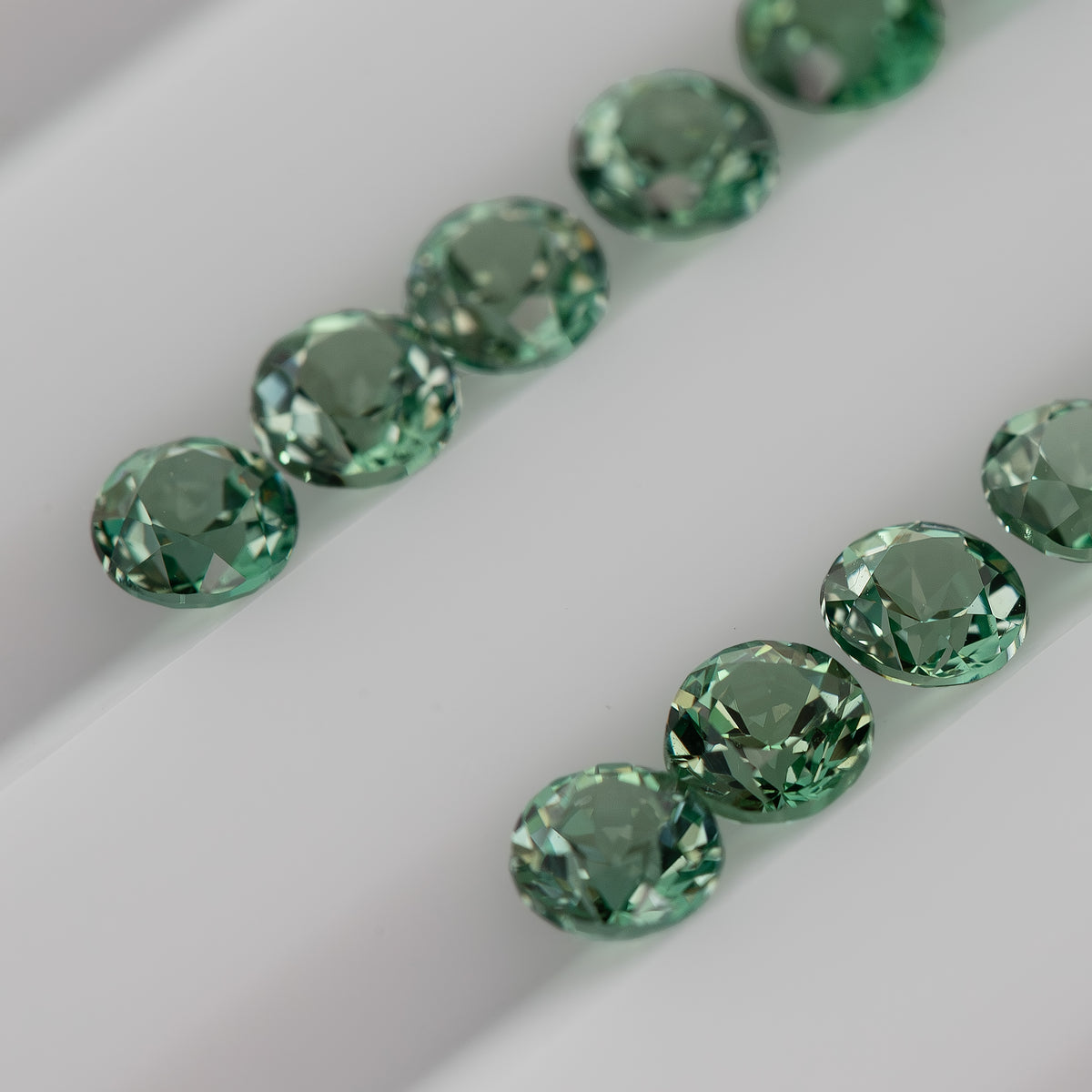 Macro view of mint-green round lab-grown sapphires arranged pavilion-up, showing pointed reverse facets.