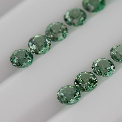 Macro view of mint-green round lab-grown sapphires arranged pavilion-up, showing pointed reverse facets.