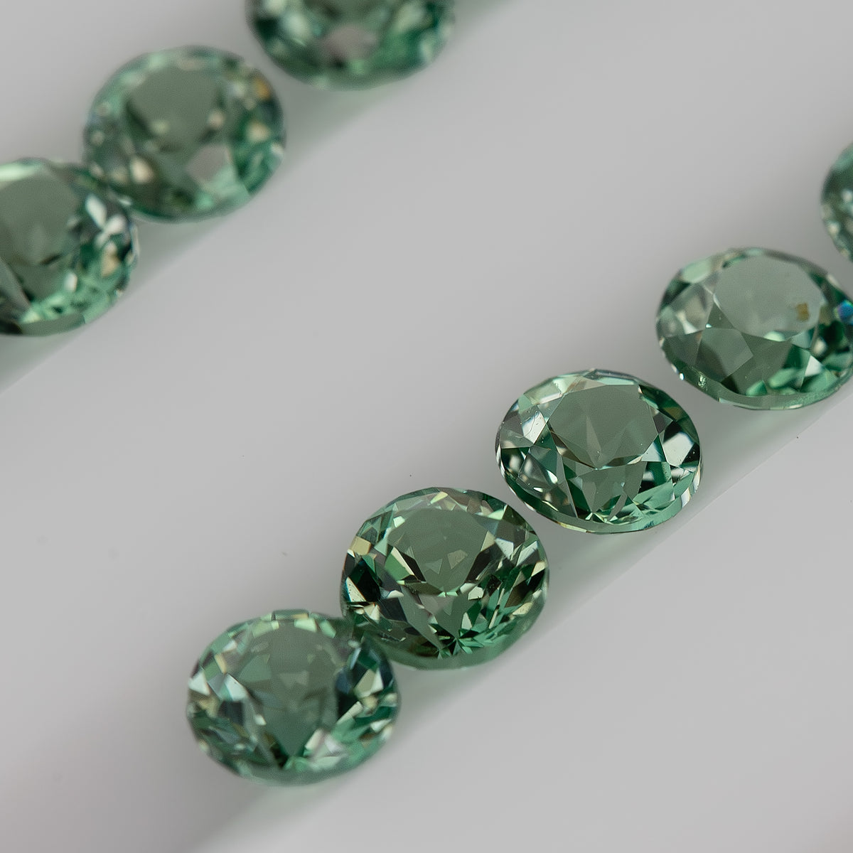 Closer reverse view of mint-green round sapphire stock with pavilion facets and pointed culets visible.