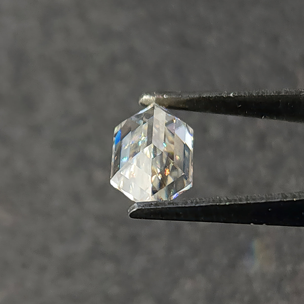 Pavilion side of a faceted hexagon cut gemstone held in tweezers displaying underside facet arrangement.