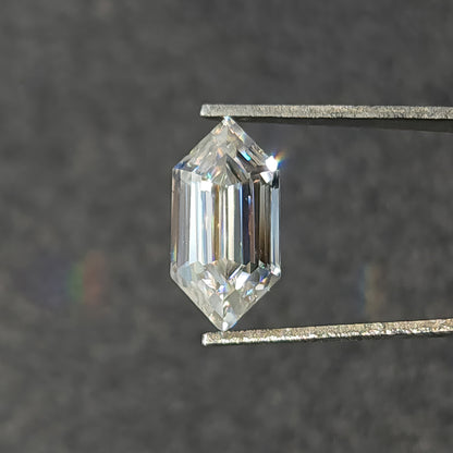 Colorless elongated hexagon cut gemstone in tweezers displaying bright internal reflections and dispersion.