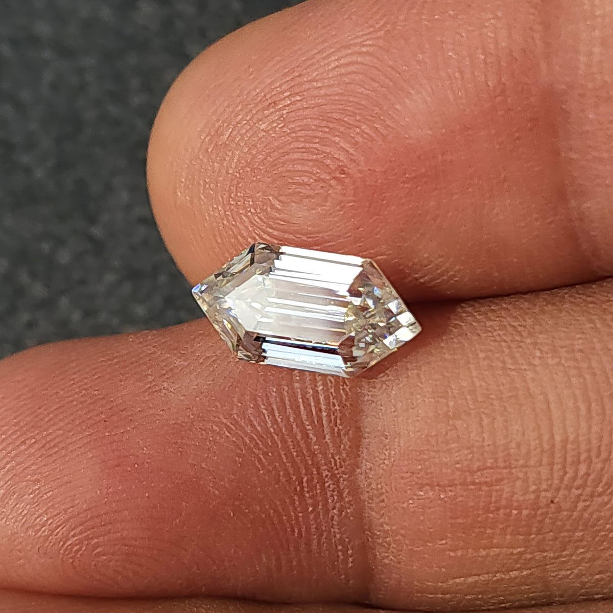 Horizontal elongated hexagon step-cut gemstone resting across fingertips illustrating hand-held scale.