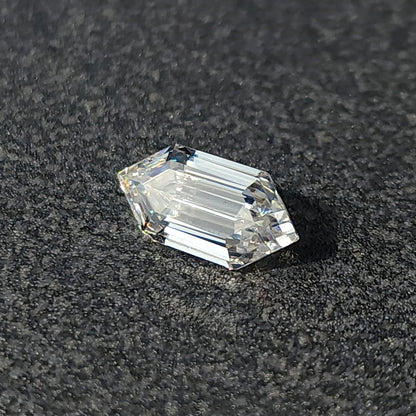 Elongated hexagon step-cut loose gem resting at an angle on a textured dark background showing light return.