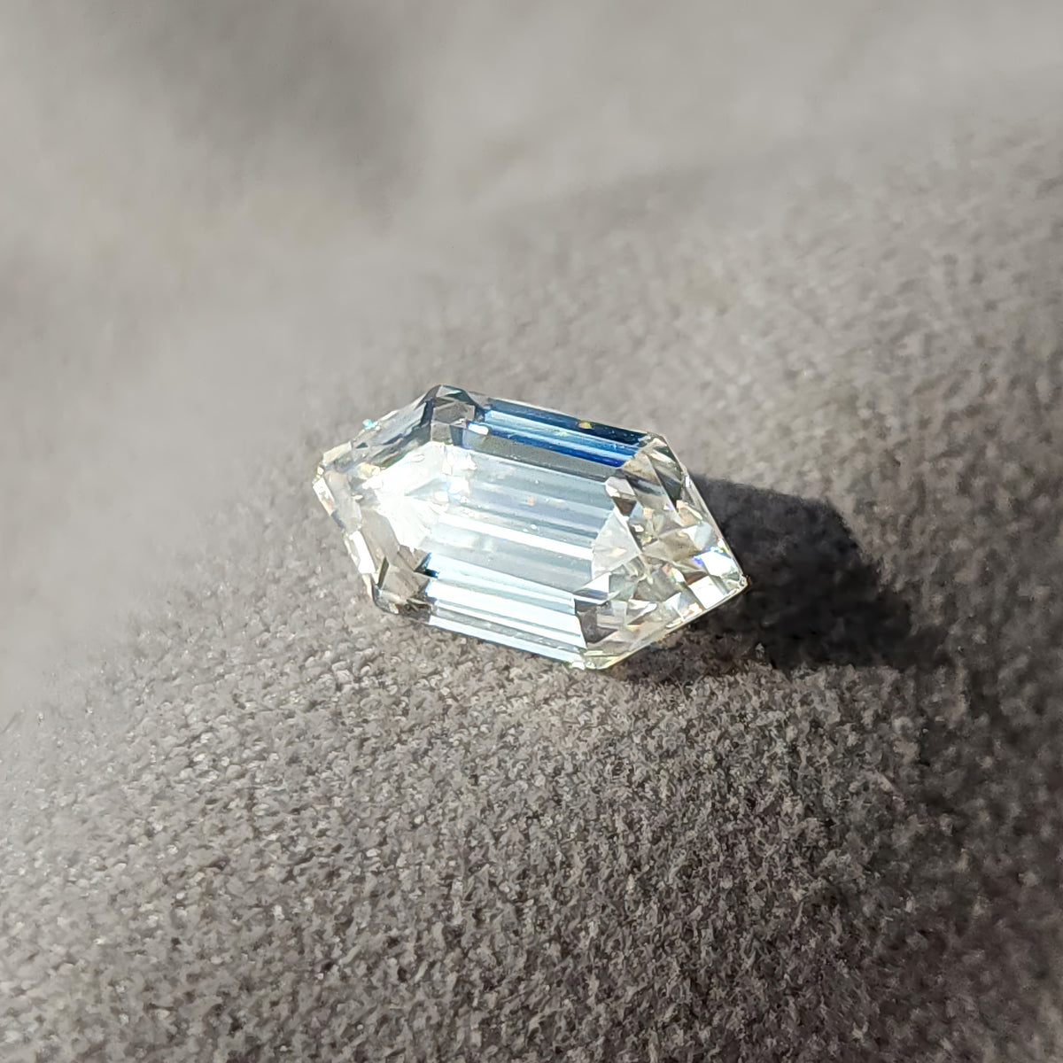 Elongated hexagon step-cut gem positioned on a light grey fabric surface displaying step facet symmetry.