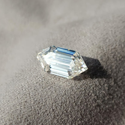 Elongated hexagon step-cut gem positioned on a light grey fabric surface displaying step facet symmetry.