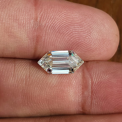 Elongated hexagon gem lying horizontally between fingertips showing scale and step-cut facets.