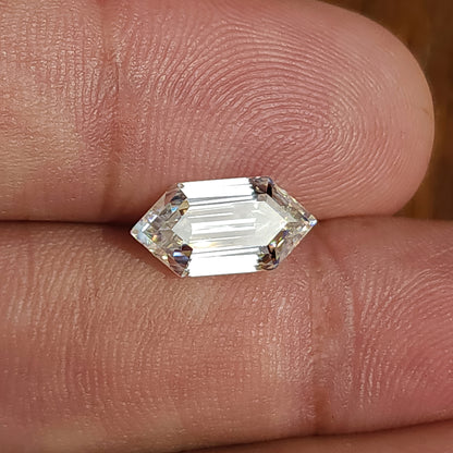 Colorless elongated hexagon step-cut stone resting on skin under strong light showing table flash.