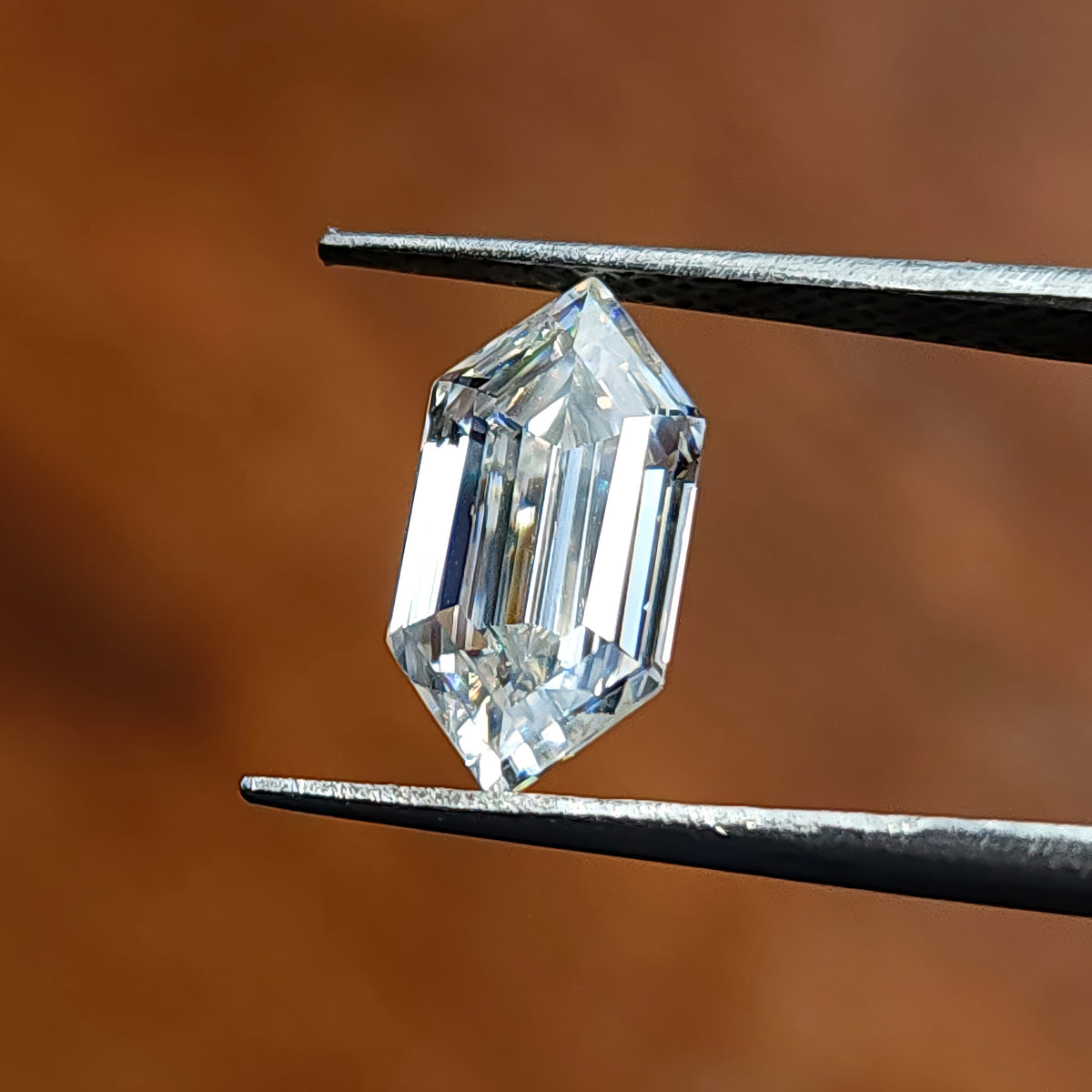 Elongated hexagon cut gem held at a slight tilt in tweezers showing parallel step facets.