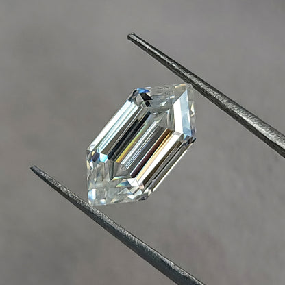 Elongated hexagon gemstone held diagonally in tweezers against a neutral grey background.