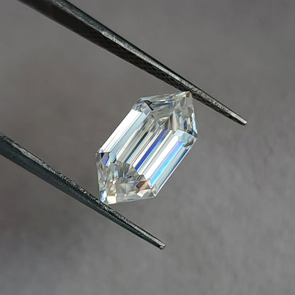 Angled view of an elongated hexagon step-cut stone in tweezers displaying facet lines and blue-violet dispersion.