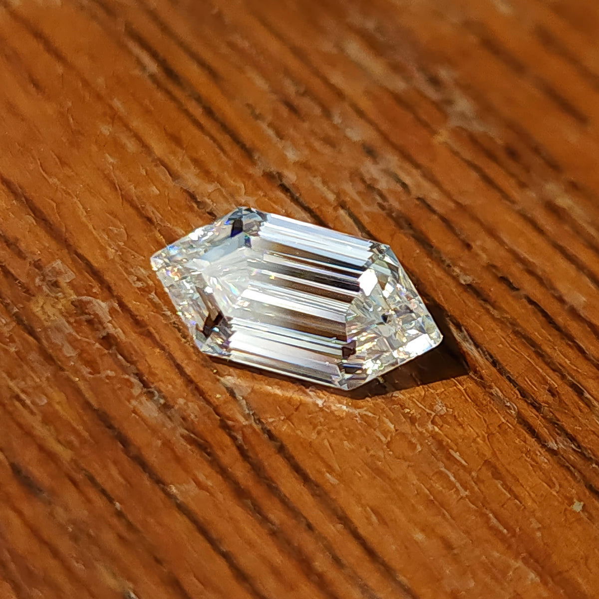 Elongated hexagon step-cut gem resting on dark grained wood surface showing facet reflections.