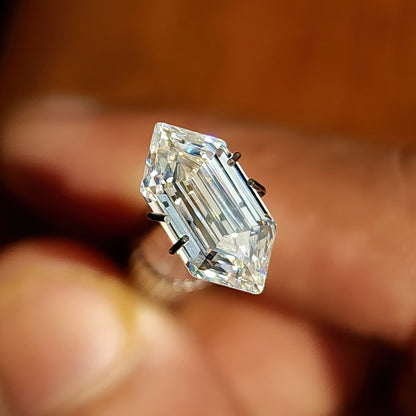 Elongated hexagon step-cut gemstone displayed in a claw prong setting holder on a hand.