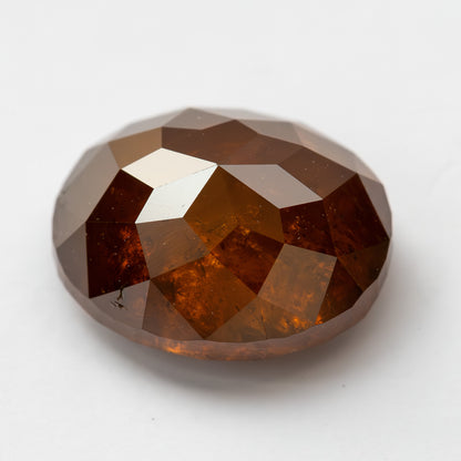 Angled loose view of the oval reddish-orange diamond on white, showing broad facets across the upper surface.