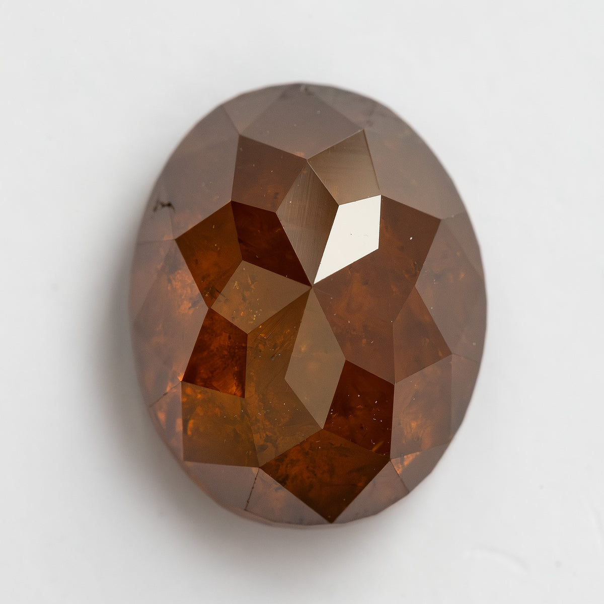 Face-up macro of the oval reddish-orange diamond on white, showing broad geometric facets and visible internal patterning.